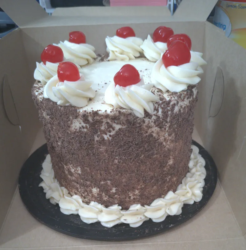 Cake coated in chocolate shavings with whipped cream rosettes and red cherries