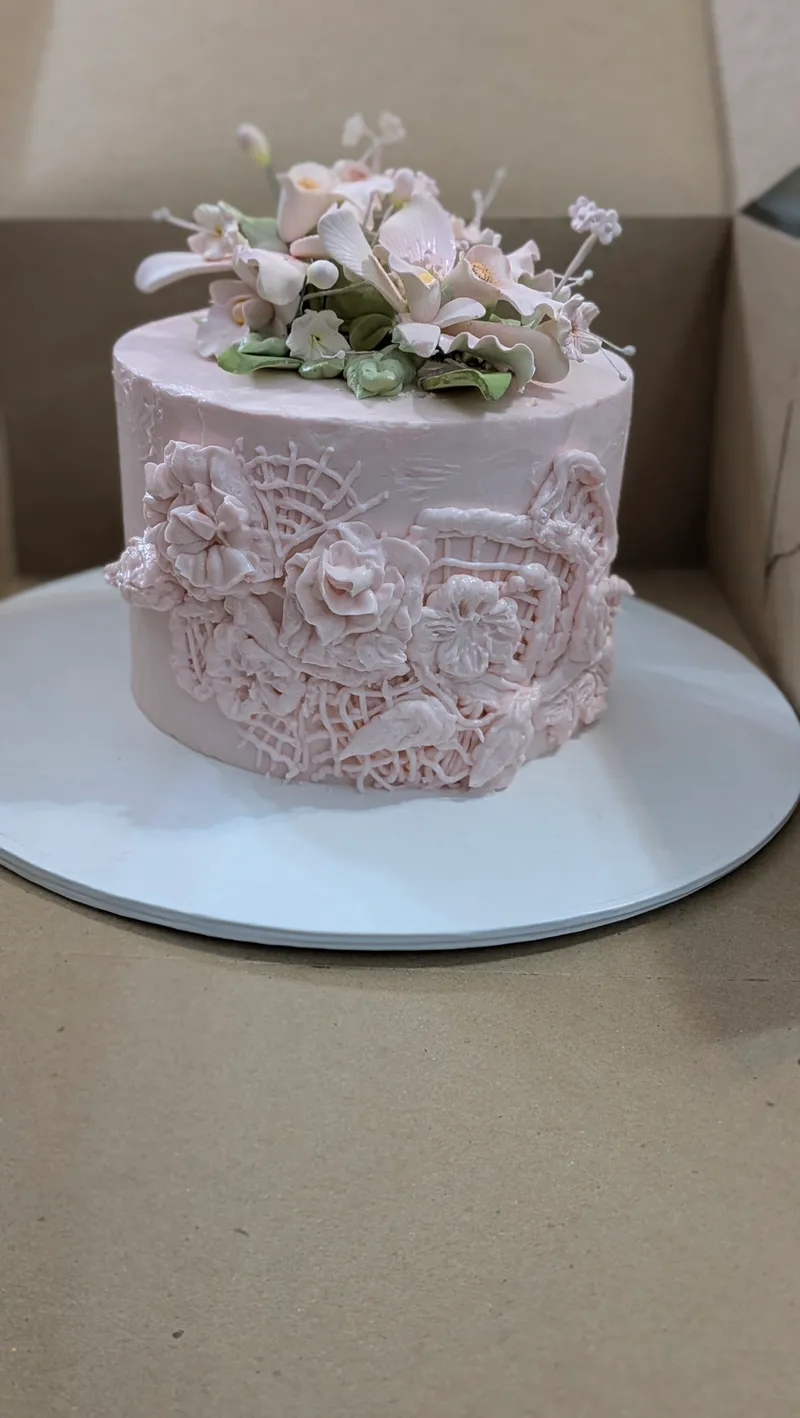 Pale pink cake with piped lace detail and a cluster of sugar flowers on top
