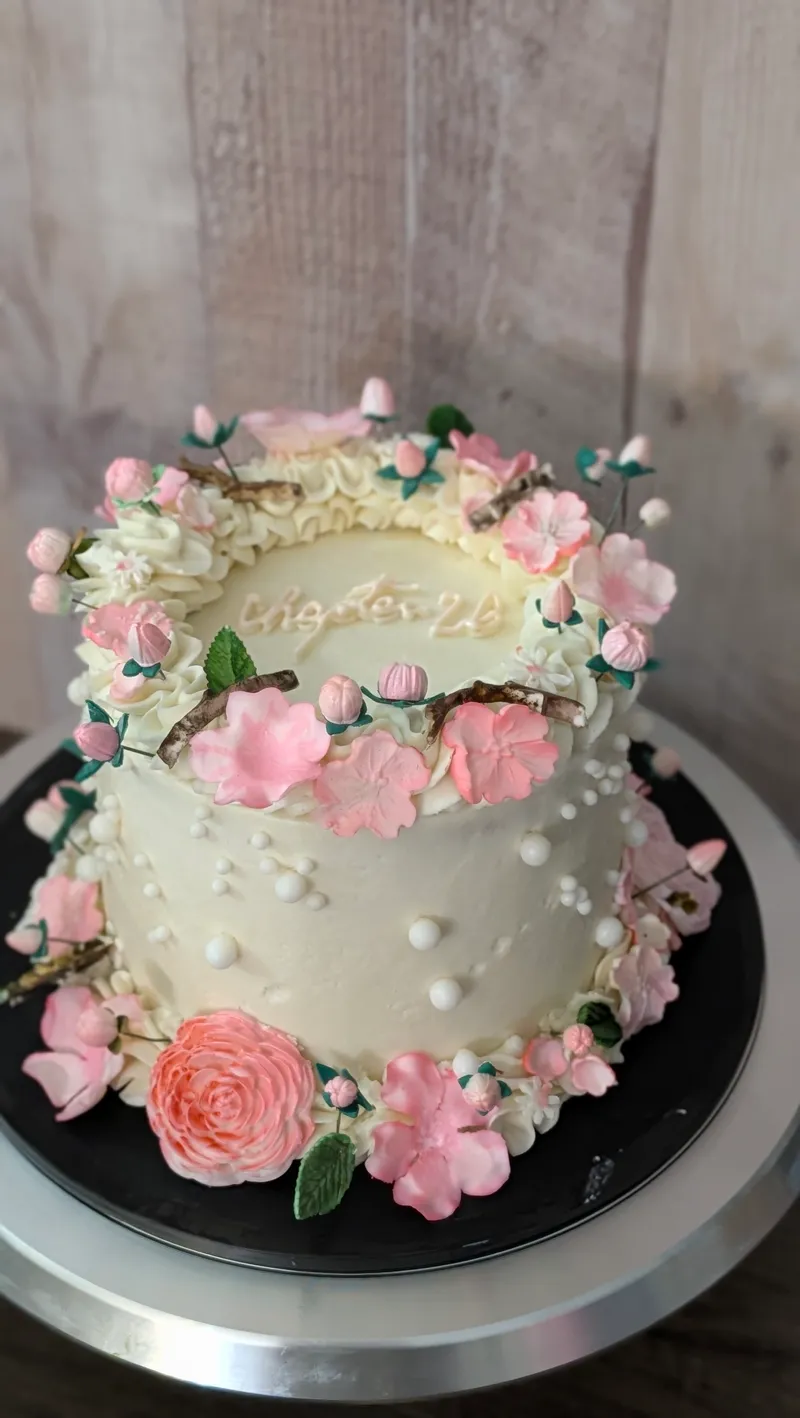 White cake with a garland of pink buttercream roses and pearl details