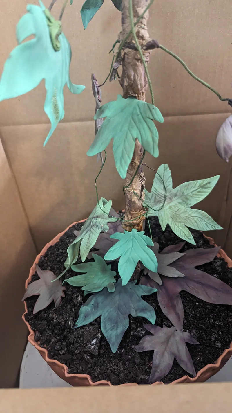 Cake sculpted as a potted plant with a vine and leaves rising from the soil