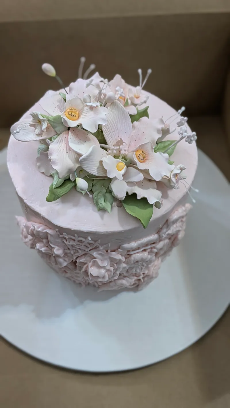Blush cake with lace-textured sides topped with a spray of white sugar blossoms
