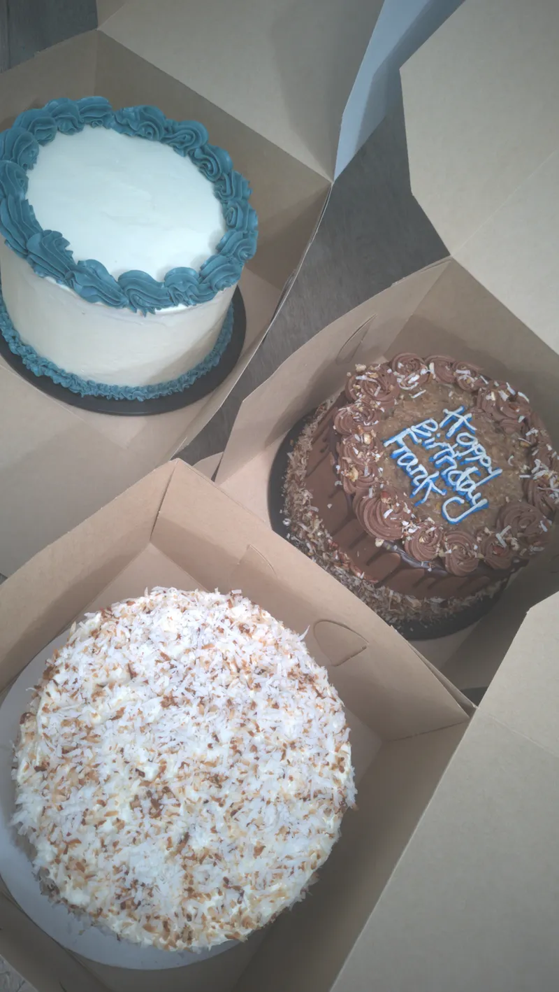 Three small boxed cakes, one white with blue piping, one chocolate and one with sprinkles
