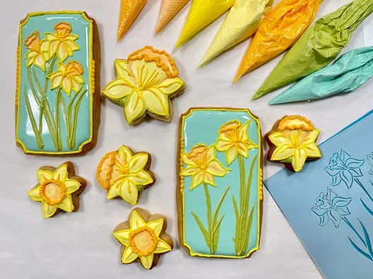 Daffodil-decorated sugar cookies beside bags of yellow and green icing