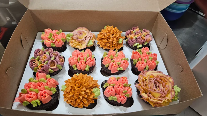 Box of cupcakes piped with orange, coral and plum flowers