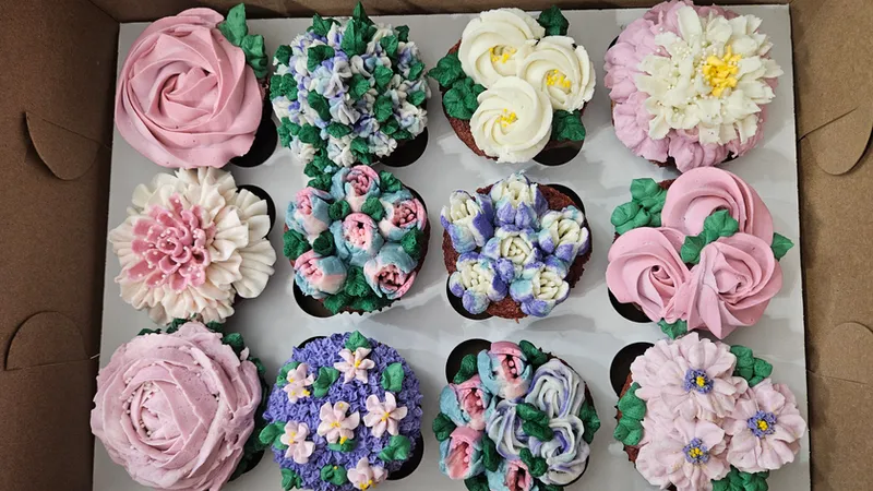 Box of cupcakes piped with pink roses, blue hydrangeas and white daisies