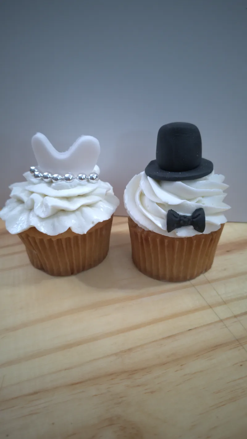 Two wedding cupcakes, one with a white dress and one with a black top hat and bow tie