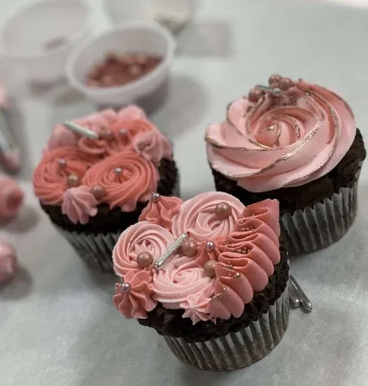 Three chocolate cupcakes with pink buttercream swirls and rose gold accents
