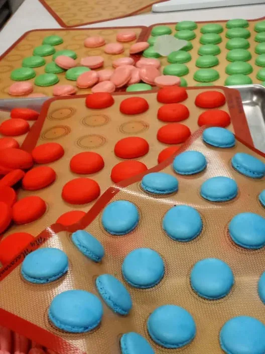 Rows of red, blue, green and pink macaron shells on baking mats
